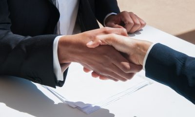 Closeup of business people shaking hands outdoors. Business man and woman wearing formal clothes and sitting at table with papers. Agreement concept.