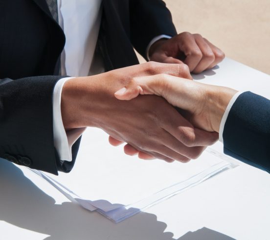Closeup of business people shaking hands outdoors. Business man and woman wearing formal clothes and sitting at table with papers. Agreement concept.