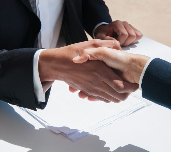 Closeup of business people shaking hands outdoors. Business man and woman wearing formal clothes and sitting at table with papers. Agreement concept.